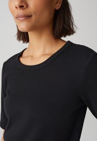 T-shirt nera a coste con scollo rotondo e maniche corte, che mette in risalto un tessuto strutturato e una silhouette aderente.