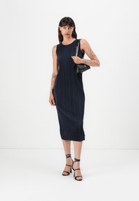 Navy ribbed midi-kjole med ærmeløs design. Kombinert med svarte sandaler med stropper og en liten svart håndveske med kjedestropper.
