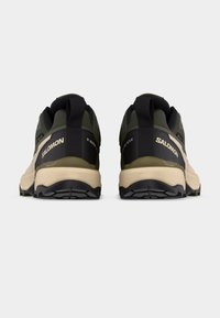 Πίσω όψη παπουτσιών τρεξίματος Salomon σε ελαιχρώματα πράσινο και μπεζ με μαύρες λωρίδες για κράτημα και ανθεκτικές μαύρες σόλες σε απλό φόντο.