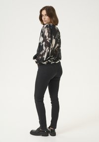 Black, long-sleeve, tie-dye blouse made of light fabric, paired with fitted black jeans and black shoes with a chunky sole.