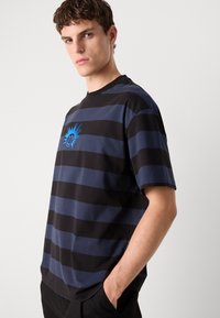 Striped T-shirt in navy and black cotton, featuring a small blue sun graphic on the chest. Short sleeves and a crew neckline.
