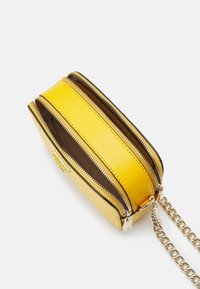 Borsa a tracolla gialla con materiale testurizzato, tre scomparti con zip e una tracolla in catena dorata. L'interno presenta una fodera in tessuto marrone.