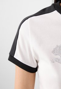 Close-up of a short-sleeved shirt featuring a white body, black sleeves, and a sparkling design on the front, revealing part of an arm.