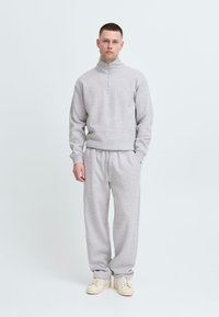 Sivela flis zip-up dukserica in ujemajoče se trenirke. Mehka tekstura, sproščen kroj. Ima rebraste manšete, pas in vrvico. Belega sneakers.