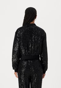 Black sequin bomber jacket with a fitted waistband and cuffs. Features a smooth collar and a textured, shimmering surface.