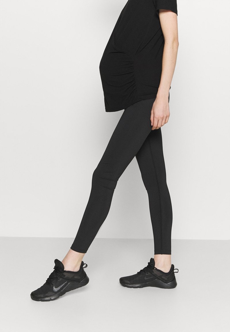 Leggings noirs avec une texture lisse et un design ajusté. Associés à un haut noir ample, portés avec des chaussures de sport noires.
