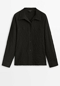 Chemise noire à manches longues boutonnée, en tissu texturé, col pointu et détails subtils des coutures sur la poitrine, présentée sur fond blanc.