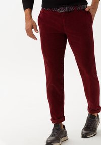 Pantalon en velours côtelé bordeaux avec une coupe slim, doté de poches latérales et de poignets retroussés, associé à des baskets grises et une ceinture tissée à motifs.