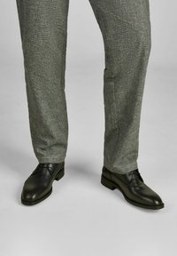 Zwarte leren nette schoenen met een gladde afwerking, gecombineerd met lichtgrijze gestructureerde broek met een subtiel ruitmotief.