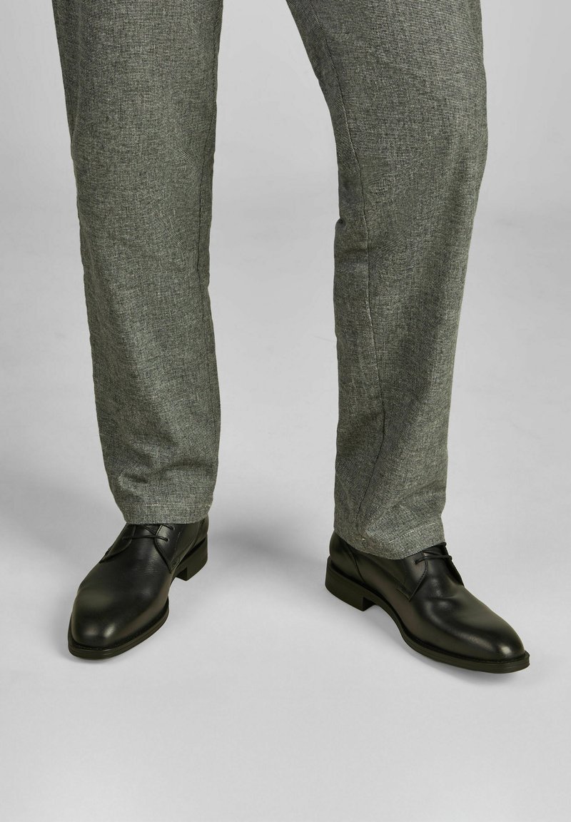 Zwarte leren nette schoenen met een gladde afwerking, gecombineerd met lichtgrijze gestructureerde broek met een subtiel ruitmotief.