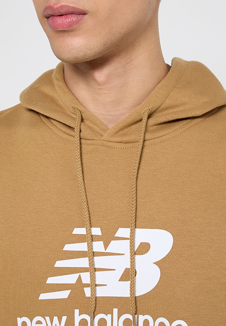 Hoodie en coton marron avec une poche kangourou, arborant un logo "new balance" en blanc. Des cordons de serrage au niveau du cou complètent le design.