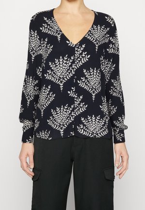 Blouse marine avec un col en V, des manches longues et une fermeture à bouton. Présente un motif de feuilles blanches. Tissu doux avec une coupe décontractée et un ourlet courbé.