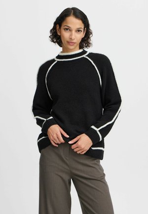 Schwarzer Strickpullover mit weißen Akzenten und gerippten Bündchen, mit hohem Kragen und Raglanärmeln. Weicher, strukturierter Stoff.