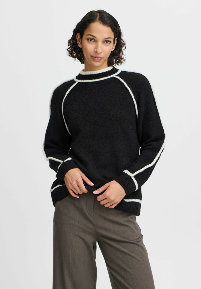 Maglione nero a maglia con accenti bianchi e polsini a coste, con un collo alto e maniche raglan. Tessuto morbido e testurizzato.