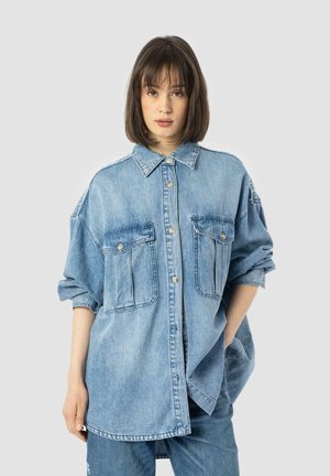 Denim shirt in light blue, featuring a button-up front, two chest pockets, rolled sleeves, and a relaxed fit.