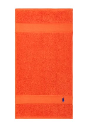 Toalla de color naranja brillante con bordes texturizados y un pequeño logo bordado en azul de un jugador de polo en la esquina inferior derecha.