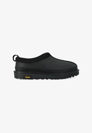 Scarpa nera senza lacci con tomaia in gomma liscia, colletto in maglia strutturata e suola Vibram con un logo giallo distintivo.