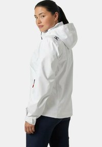 Chaqueta blanca impermeable con capucha, que cuenta con un bolsillo con cremallera en la manga, tejido transpirable y detalle de logotipo en la parte posterior.