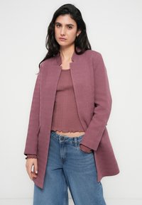 Μπλέιζερ σε χρώμα δαμάσκηνου με υφή, γιακά μανδαρίνου και ανοιχτό μπροστινό μέρος, φορεμένο πάνω από το αντίστοιχο ριμπ πλεκτό τοπ και τζιν παντελόνι με ψηλή μέση και χαλαρή γραμμή.