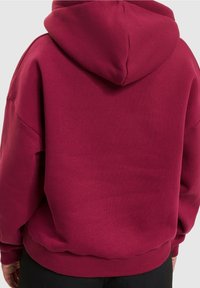 Bordeauxroter Hoodie aus weichem Stoff, mit großer Kapuze, langen Ärmeln sowie gerippten Bündchen und Saum. Glatte Textur, minimalistische Details.