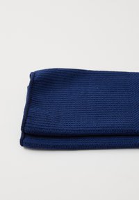 Marinblått stickat tyg vikt på mitten, med ett strukturerat ribbmönster. Materialet verkar mjukt och elastiskt.