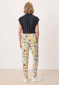 Zwarte blouse met korte mouwen en een kraag, gecombineerd met lichtgekleurde bloemenpatroonbroek in geel, blauw en paars, gedragen met witte sneakers.