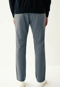 Chino gri din bumbac, cu un design drept, caracterizat printr-o textură netedă și detalii minime de cusătură, asortat cu adidași albi.
