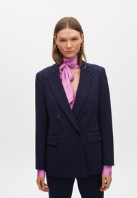 Blazer doppiopetto blu navy con decorazioni sulle spalle, dotato di sciarpa al collo in satin rosa e maniche lunghe con polsini rosa.