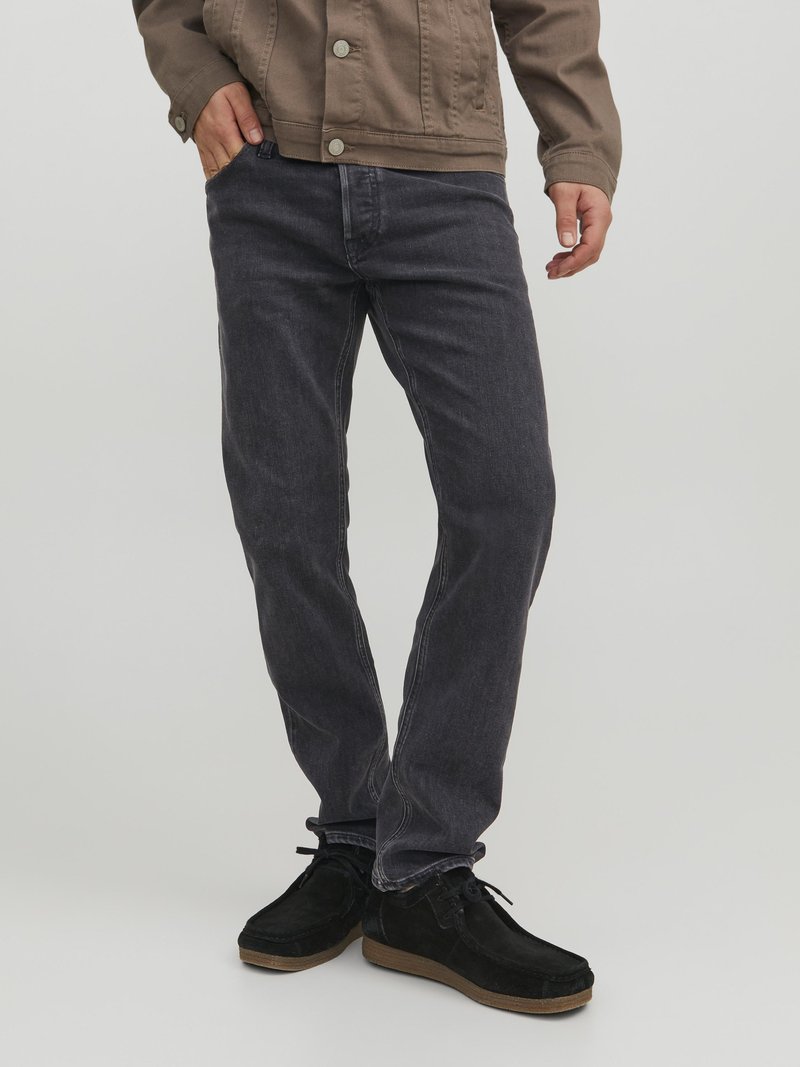 Jeans en denim gris foncé avec une coupe droite, associés à des chaussures en daim noires. Coutures visibles et poches avant. Design décontracté.