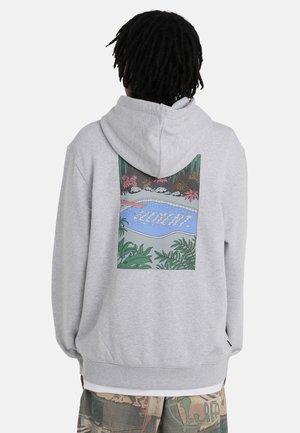 Persoon met dreadlocks die een lichtgrijze hoodie draagt met aan de achterkant een kleurrijke zwembadscène met duikplank en omliggende planten.