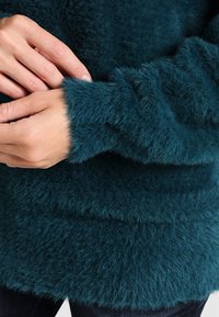 Luddig tealtröja med mjuk textur, försedd med långa ärmar och rundad halsringning. Lämplig för avslappnad användning.