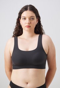 Musta saumaton bralette leveillä olkaimilla, pyöreällä pääntiellä ja sileällä, joustavalla kankaalla. Suunniteltu mukavuutta ja tukea varten minimalistisella ilmeellä.