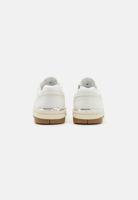 Baskets en cuir blanc au toucher lisse, dotées d'une semelle en caoutchouc beige et de détails arrière. Accent logo métallique sur le talon.