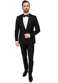 Zwarte smoking met satijnen revers, witte overhemd en zwarte vlinderstrik. Slim-fit broek, gepolijste zwarte schoenen en subtiele details op de mouwen.