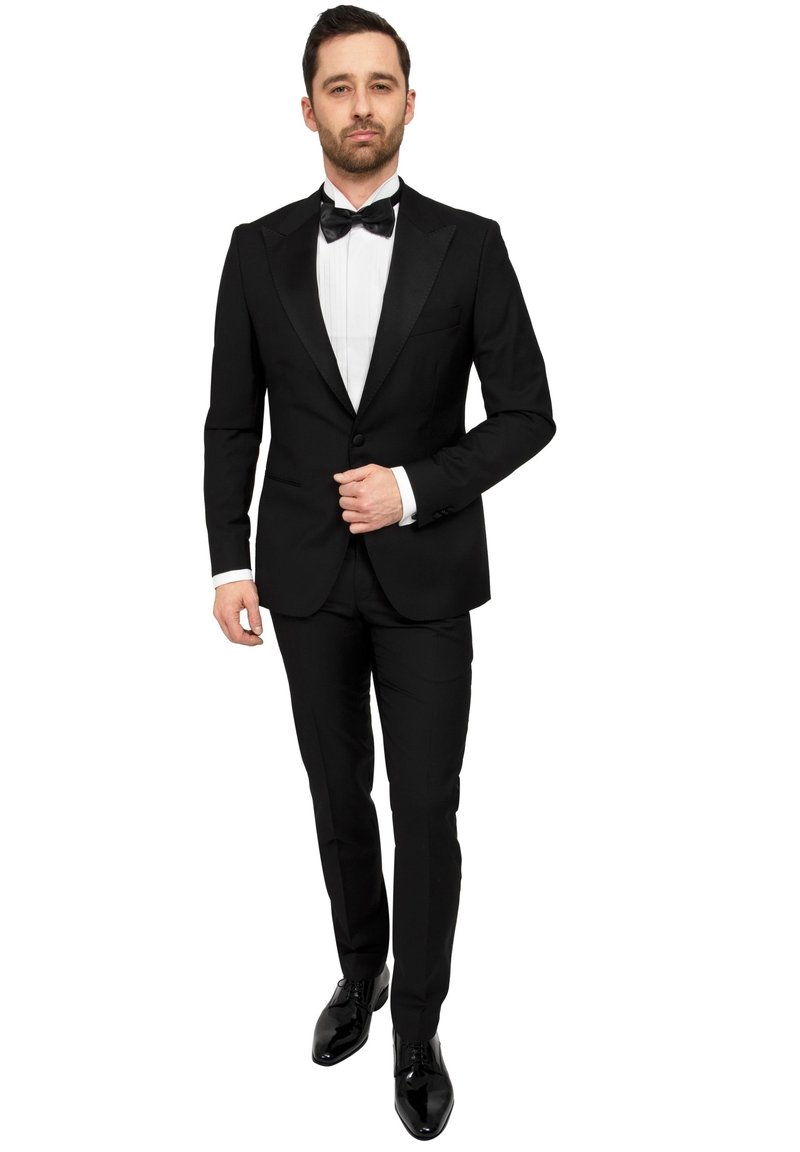 Zwarte smoking met satijnen revers, witte overhemd en zwarte vlinderstrik. Slim-fit broek, gepolijste zwarte schoenen en subtiele details op de mouwen.