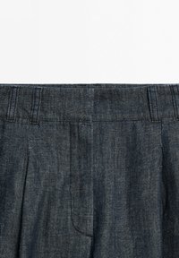 Dark blue denim pants waistband with belt loops and pleats, shown against a white background.