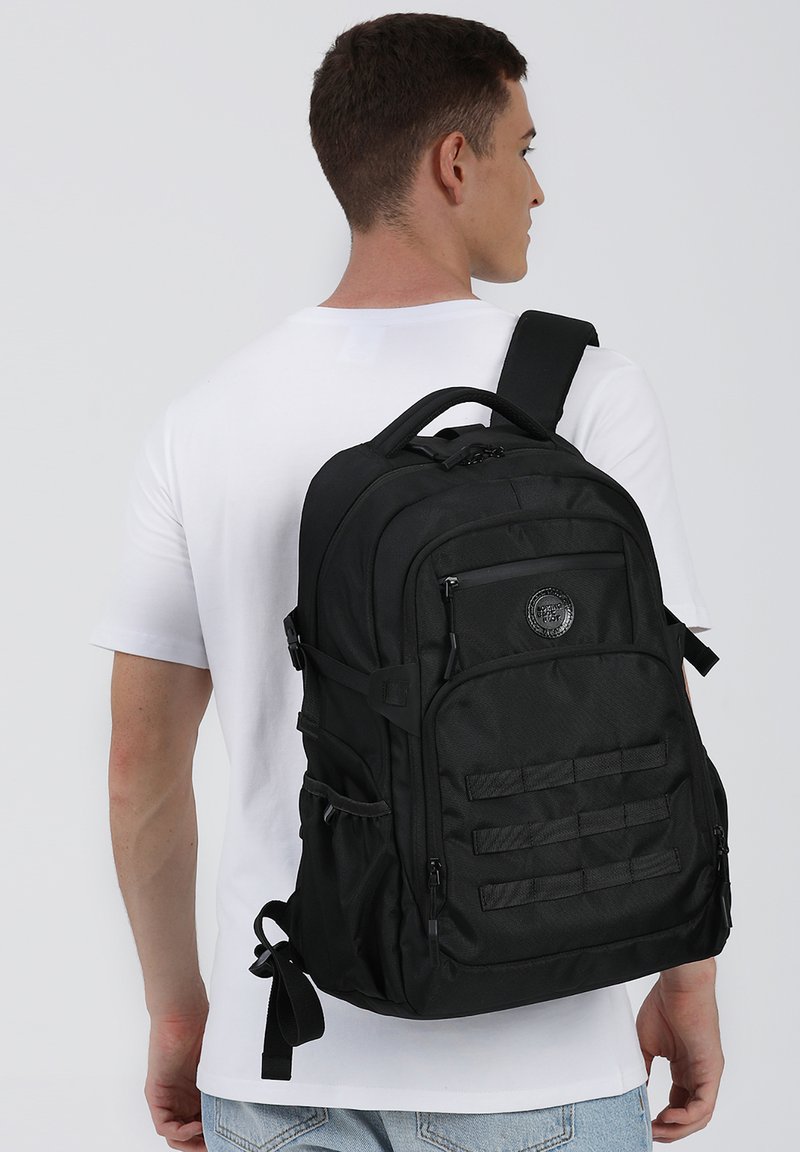 Sac à dos noir avec une finition texturée, plusieurs compartiments, des bretelles ajustables et un logo circulaire. Conçu pour la fonctionnalité et la durabilité.