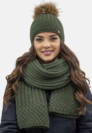 Bonnet tricoté vert olive avec un pompon en fausse fourrure et une écharpe texturée assortie, présentant un design côtelé et un fil doux et épais.