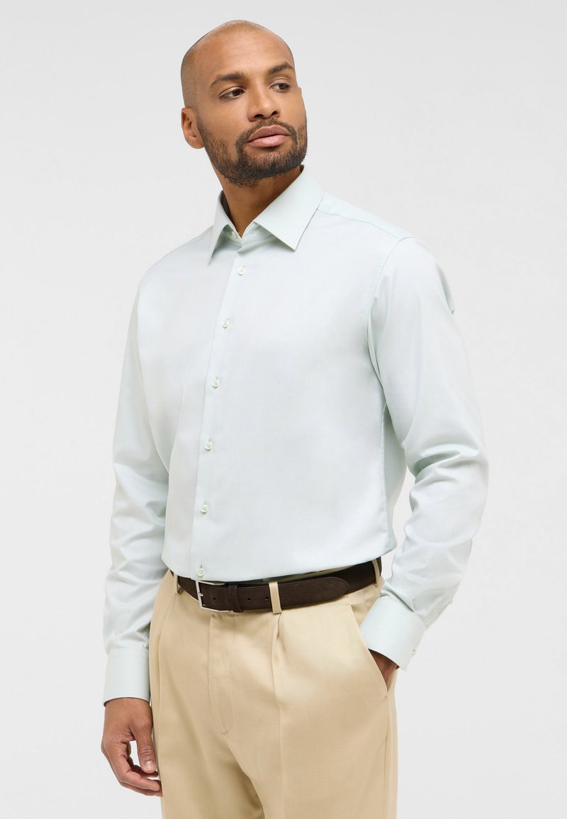 Lichte mintgroene blouse met lange mouwen, een button-down kraag en een subtiele textuur, gecombineerd met beige broeken en een leren bruine riem.
