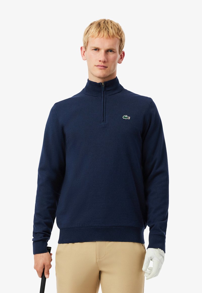 Pull de mi-zip bleu marine en tissu doux, avec un col et des poignets côtelés, portant un petit logo vert sur la poitrine.