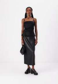 Top peplum de satén negro con tirantes finos, combinado con una falda midi de cuero negro y zapatos de plataforma gruesos. Sosteniendo un bolso negro.