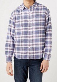 Camisa de franela a cuadros con una paleta de colores púrpura y azul, con botones en la parte delantera y bolsillo en el pecho. Textura suave y corte relajado.