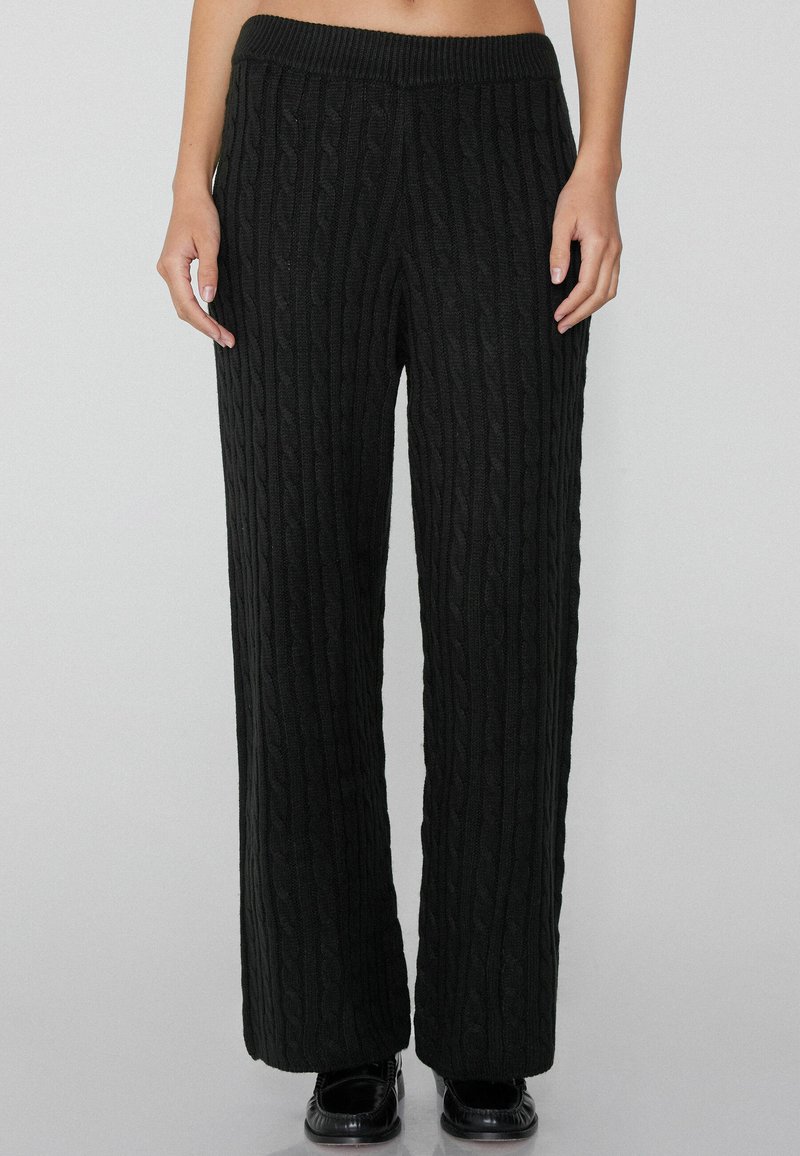 Zwarte kabelgebreide wijde broek met een geribbelde elastische tailleband. De stof heeft een gestructureerd patroon, wat zorgt voor een comfortabele en losse pasvorm.