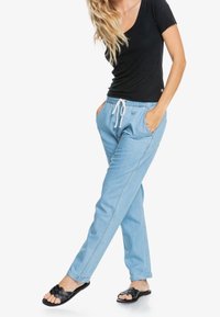 Pantaloni jogger azzurri chiari con cintura elastica e cordino bianco, dotati di tasche laterali e vestibilità rilassata. Abbinati a un top nero.