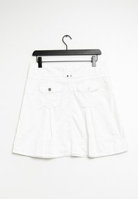 Jupe en coton blanche au design évasé, dotée de deux poches avant, de fermetures à pression, et d'un motif texturé subtil. Accrochée à un clip noir.