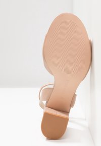 Chaussure à talon beige avec une semelle texturée, design à dos ouvert et fines lanières. Surface lisse et marquage subtil sur la semelle.