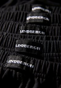 Zwarte stof met een geplooide textuur, met meerdere zwarte labels waarop "LINDENGRTH" in witte letters staat en die stiksels tonen.