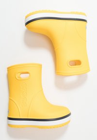 Bottes de pluie en caoutchouc jaunes avec une texture lisse, un design arrondi et une bande blanche et noire sur la semelle. Comprend une sangle au talon et un logo.