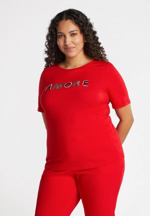 Rode T-shirt met korte mouwen met "AMORE" in rhinestones op de borst. Gladde stof met een ontspannen pasvorm. Gecombineerd met bijpassende rode broek.