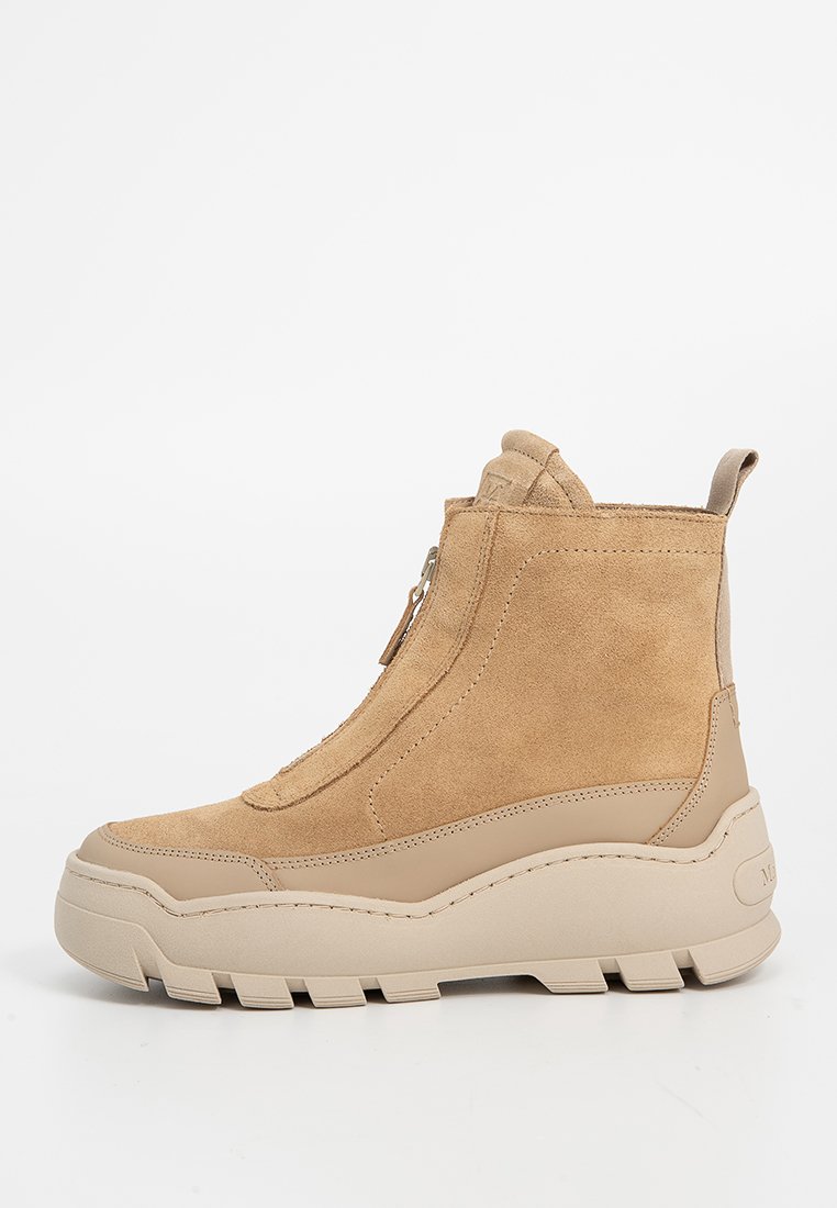 Botas de tobillo de ante en tono marrón claro con suela gruesa beige, que cuentan con una cremallera lateral y una lengüeta trasera para facilitar su uso.